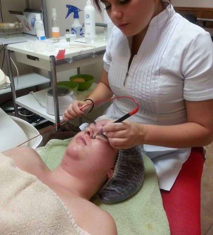 A woman receiving an electrolysis treatment on her face at a spa. A technician holds tools, performing the procedure.