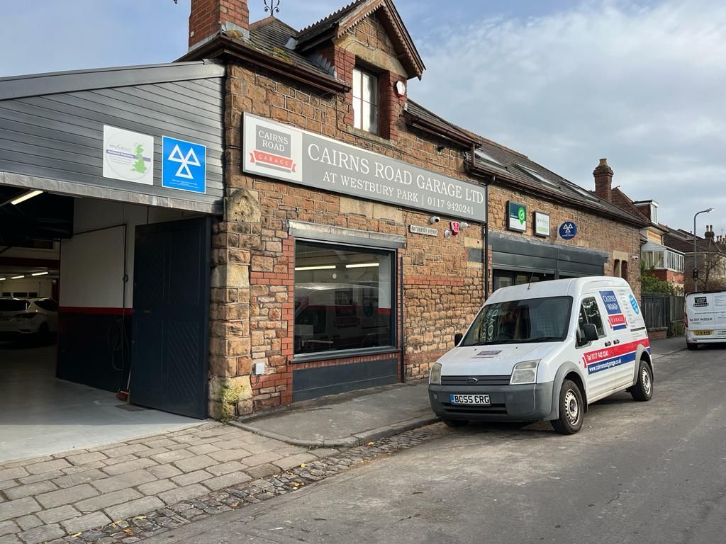 A brick building with a garage door open and a white service van parked in front.