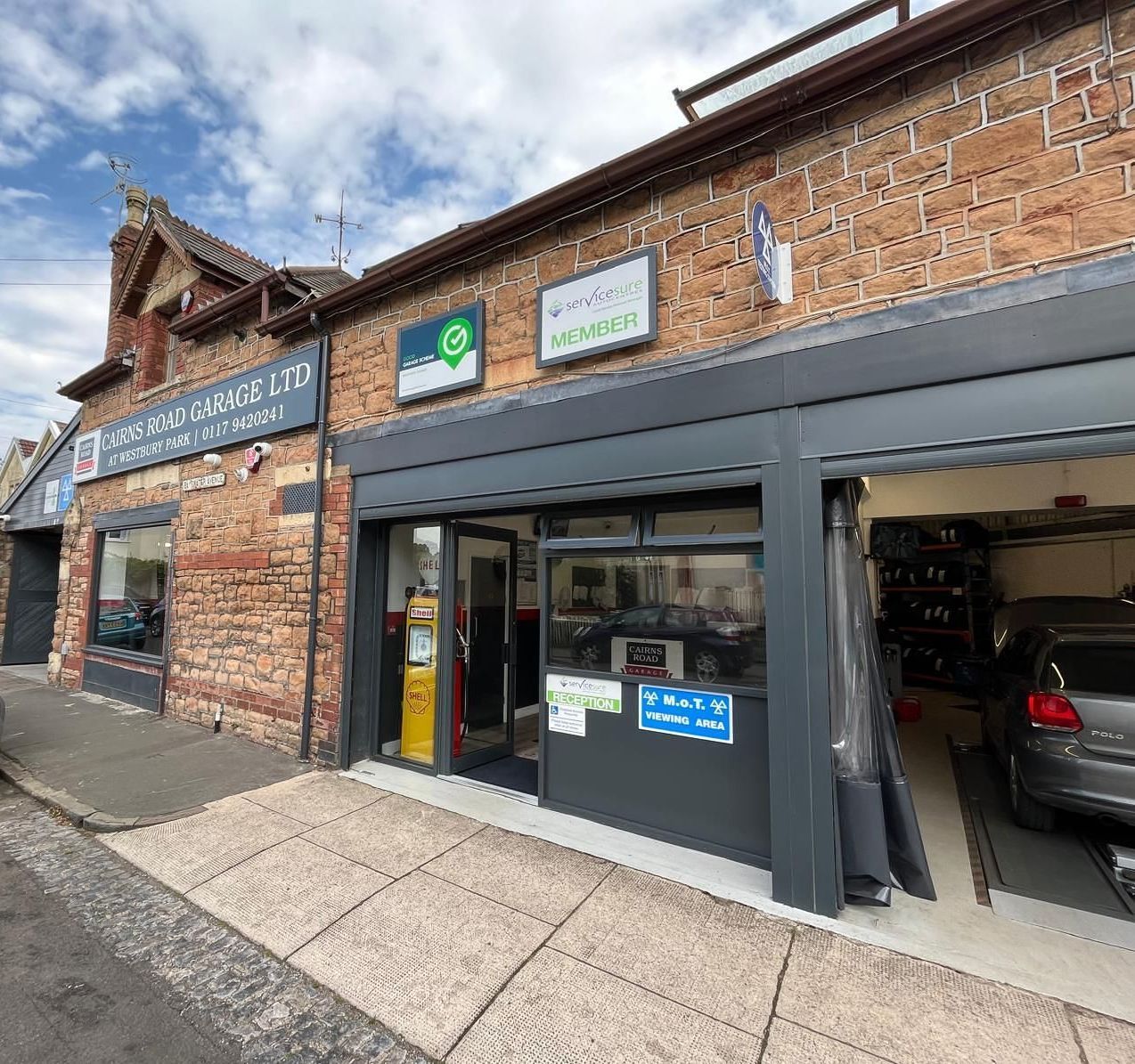 Exterior of an auto repair shop with brick facade. Open garage door reveals a car inside.