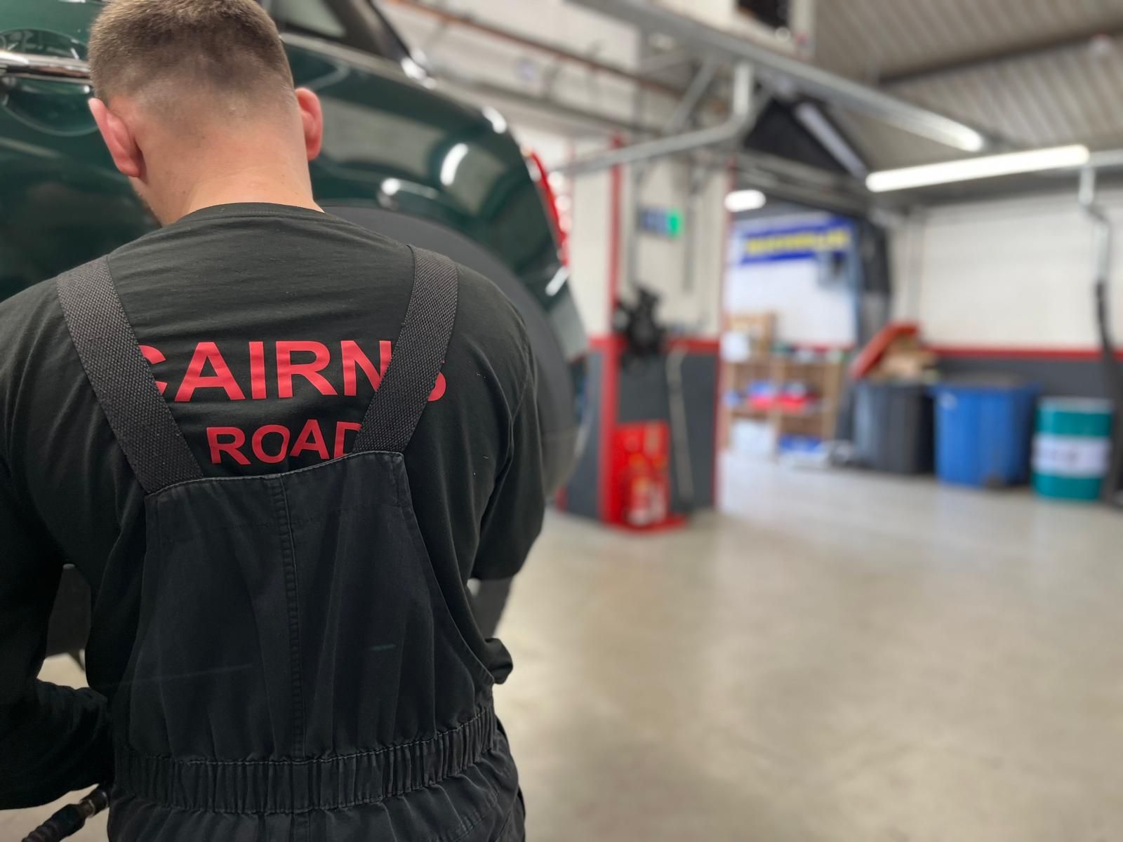 Mechanic working on a car in a garage, wearing a black jumpsuit.  