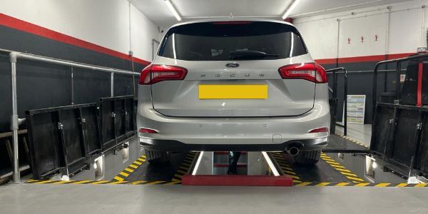 Silver car on a lift in a garage, yellow license plate, black and red trim.