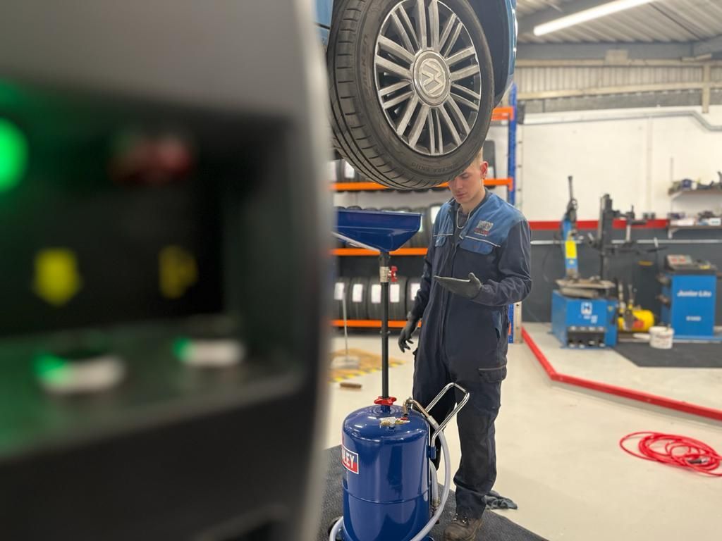 Mechanic working on a car on a lift in a garage, using a tablet, with oil drain.