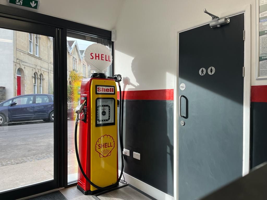 Shell gas pump inside a building with a black and red accent wall, a door, and an open glass door to the street.
