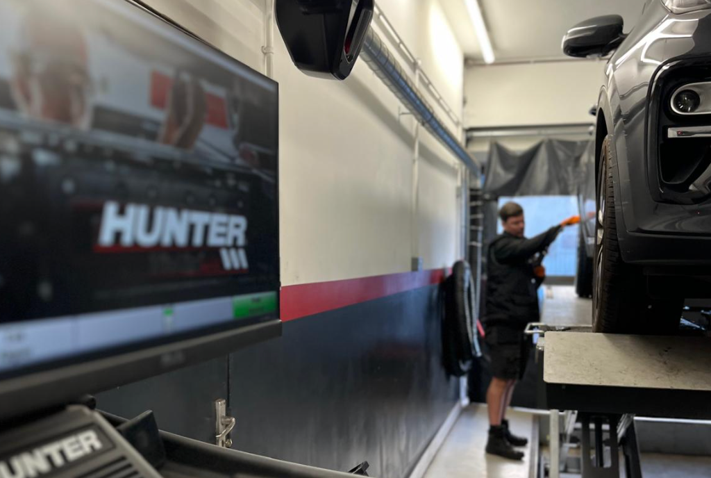 Mechanic adjusting car wheel with Hunter alignment system display in auto shop.