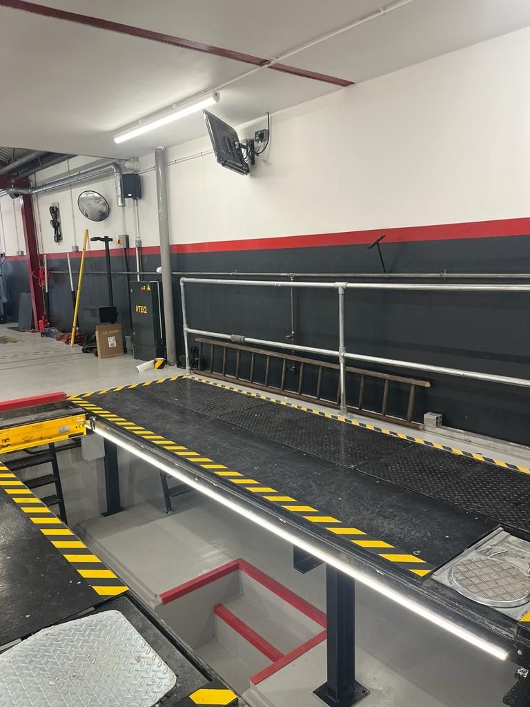 A vehicle service bay with a car lift, safety barriers, and tools in a garage setting.