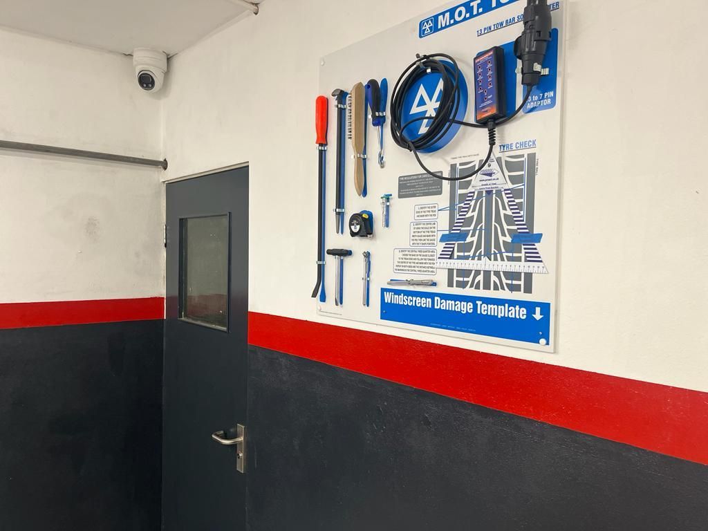 Wall-mounted tool display with various instruments next to a gray door and red-trimmed black wall.