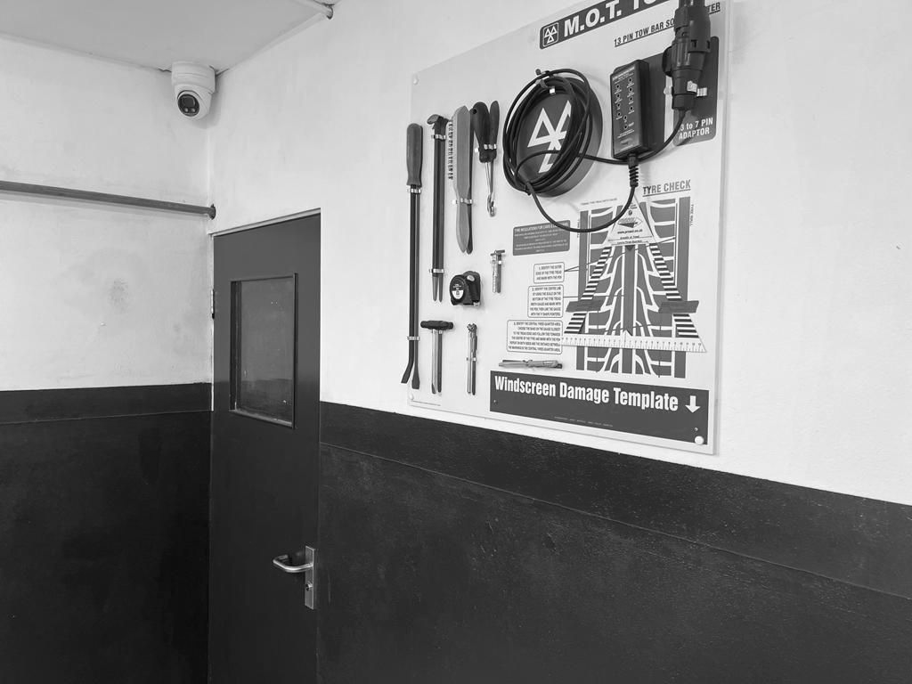 Black and white photo of a poster with tools and diagrams, mounted on a wall near a door and a security camera.