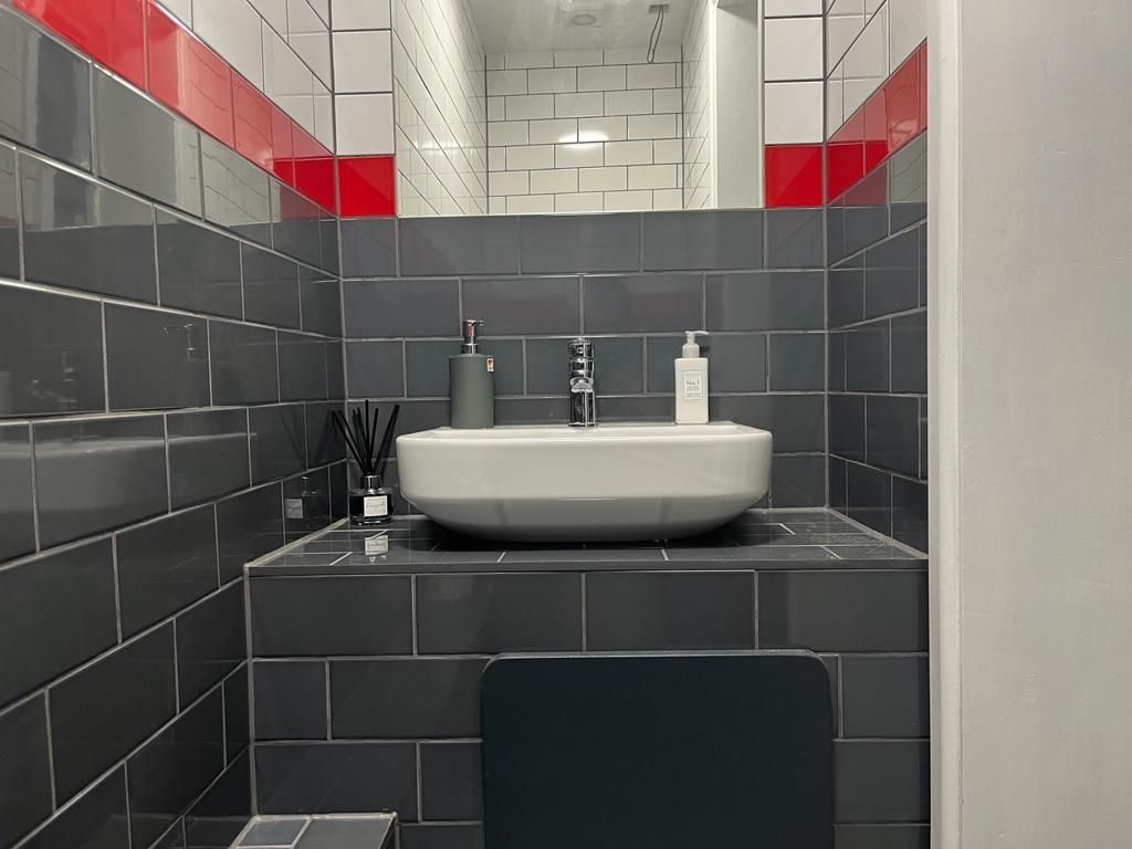 Bathroom with gray tiled walls, a white sink, and red accent stripes.