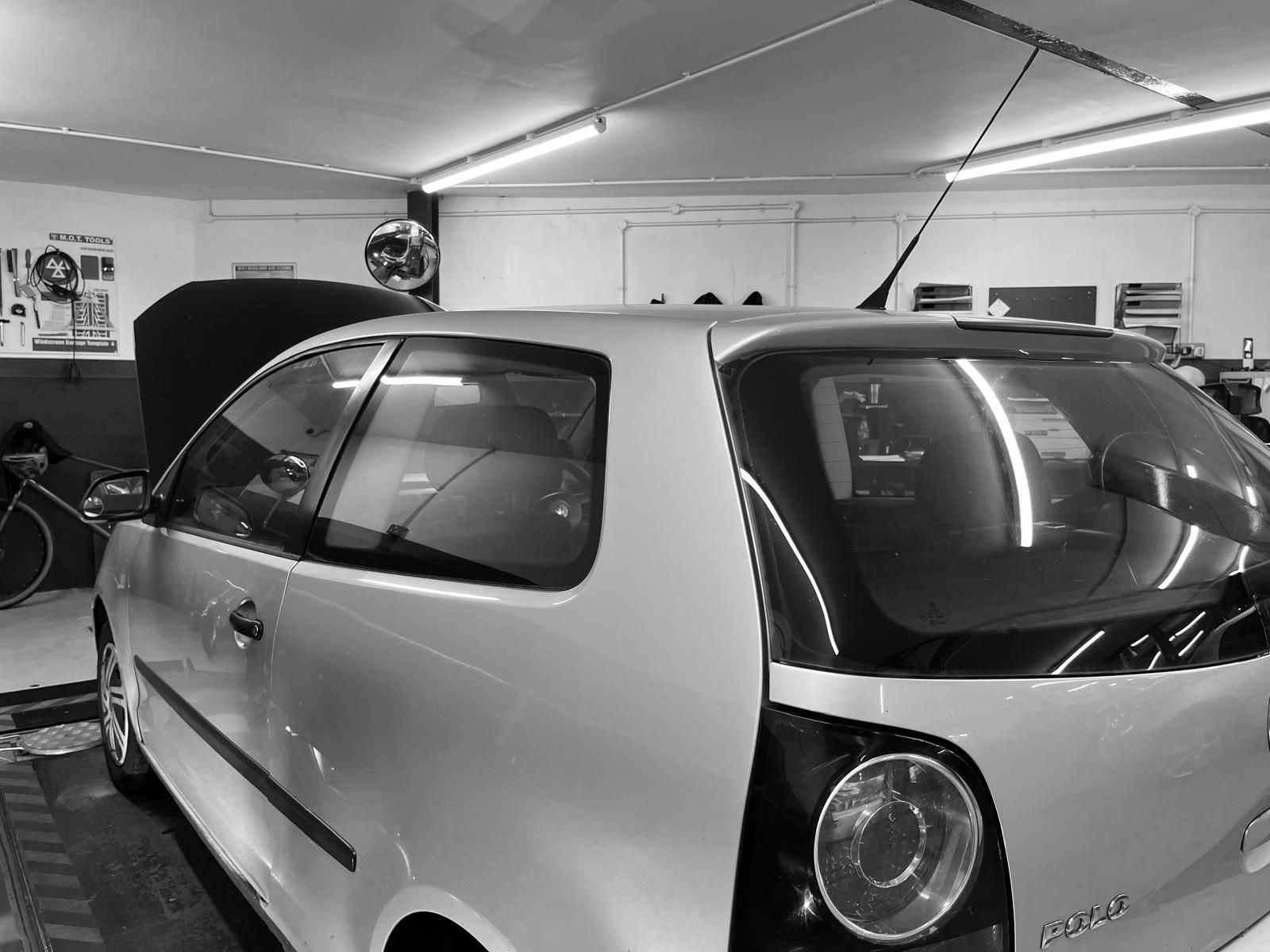 Silver hatchback car in a garage with hood open, under fluorescent lights.