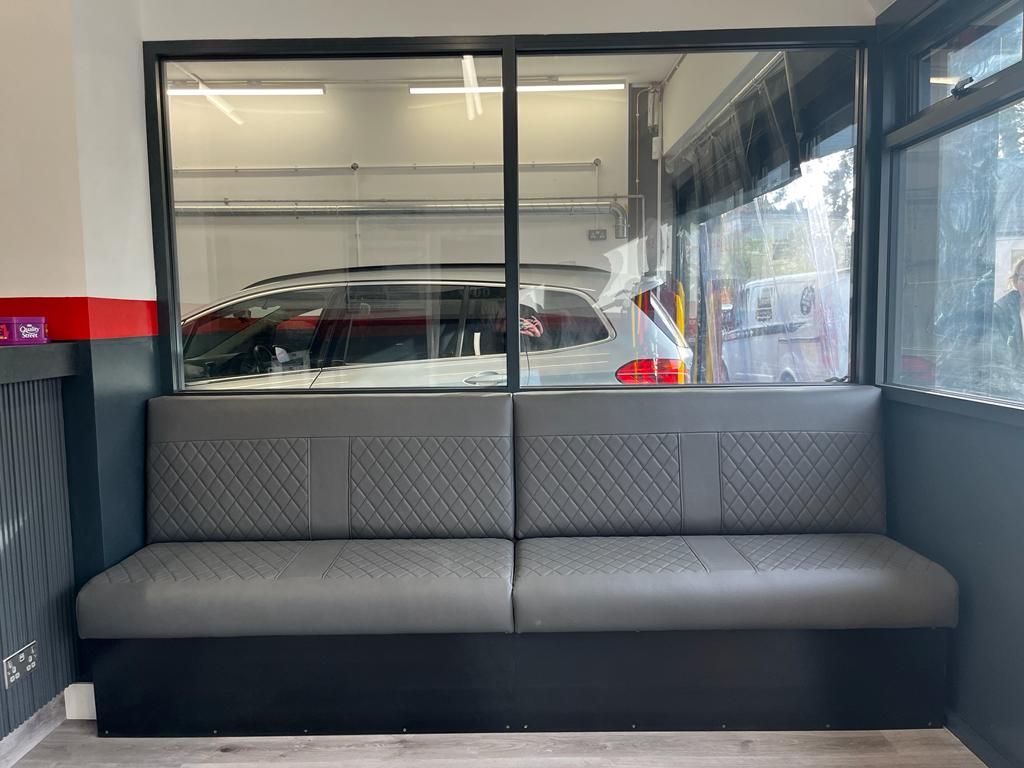 Gray bench seat in waiting area, with large window view of a car wash bay.