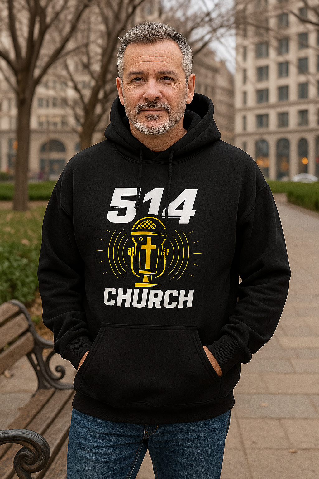 Man standing in a park wearing a black hooded sweater. the hood is down and he is posing for a frontal photo