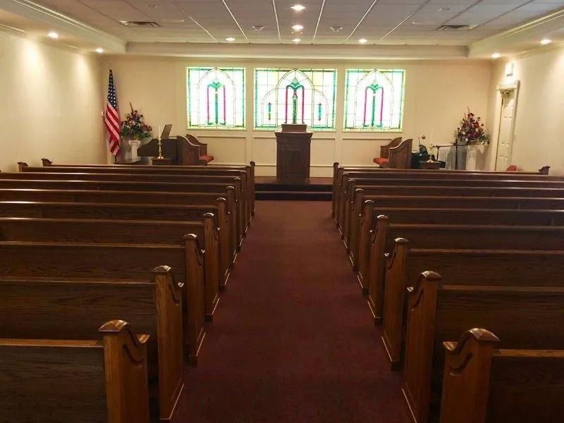 Interior view of a church sanctuary with wooden pews, a podium, and stained-glass windows.