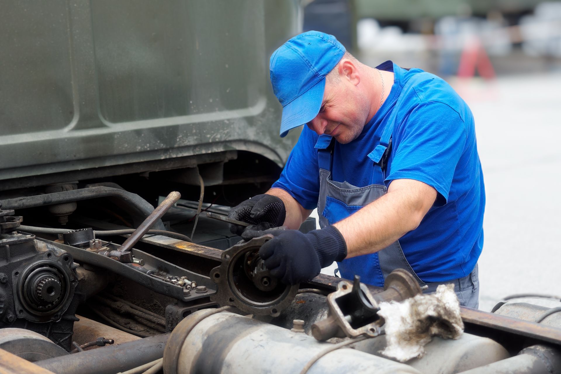 Mechanic in blue overalls working on a truck engine, outdoors.