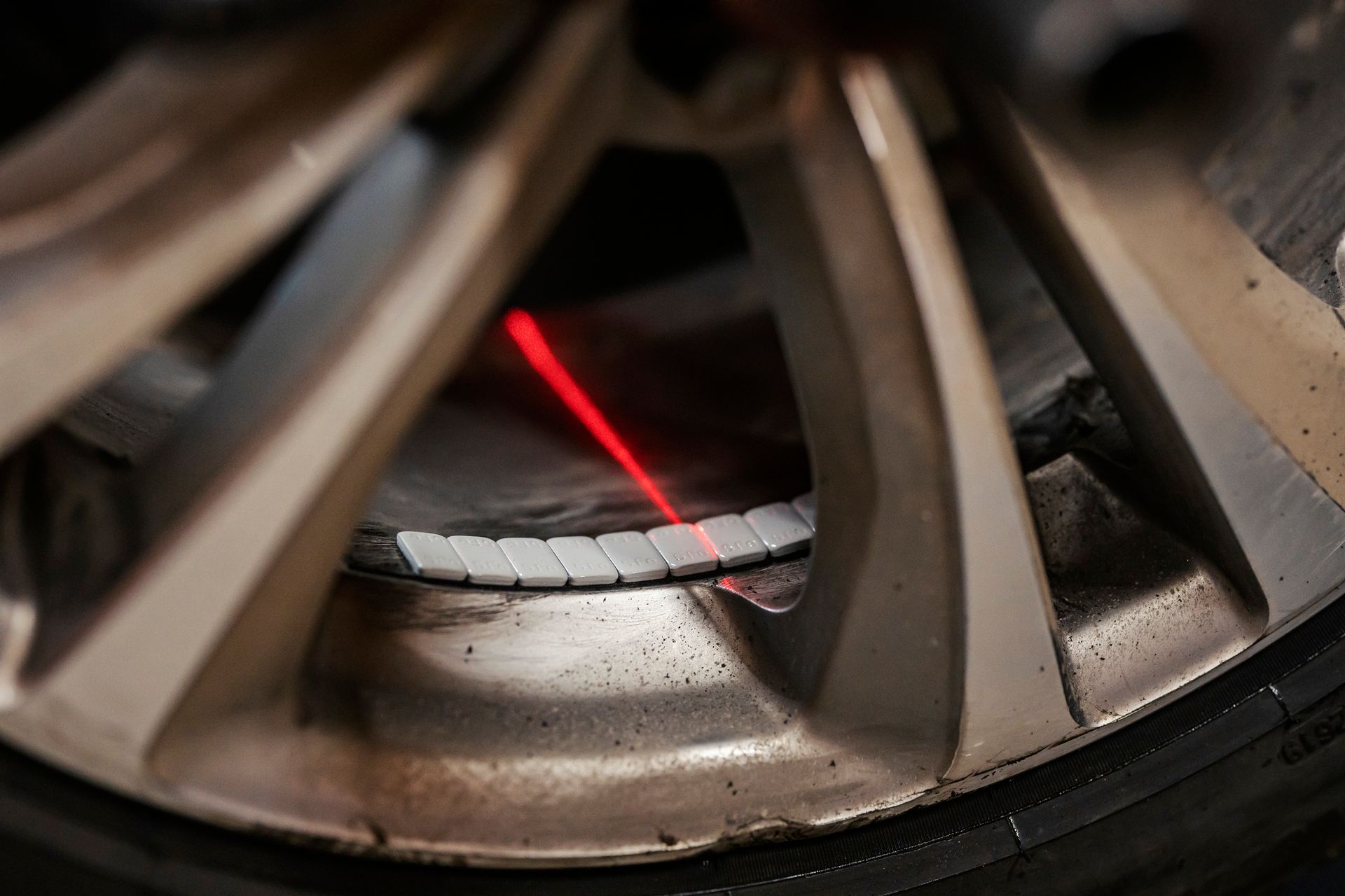 A car wheel with silver rim, balancing weights, and a red laser beam for alignment.