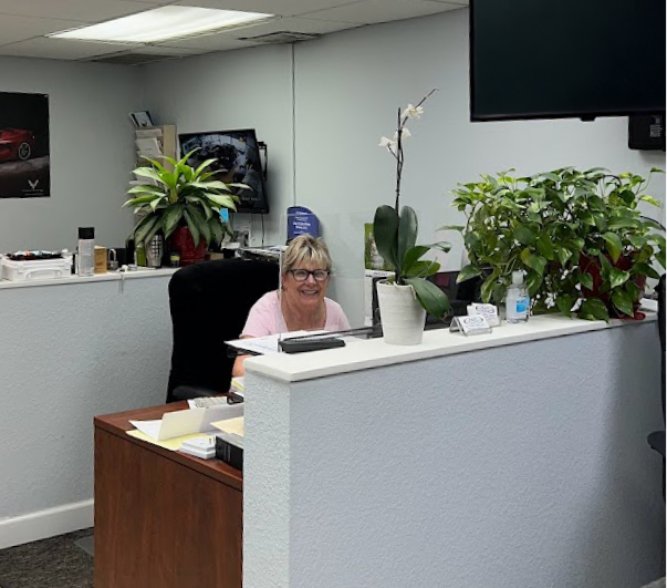 A woman sits at a desk in an office surrounded by plants | B & R Auto Body Works