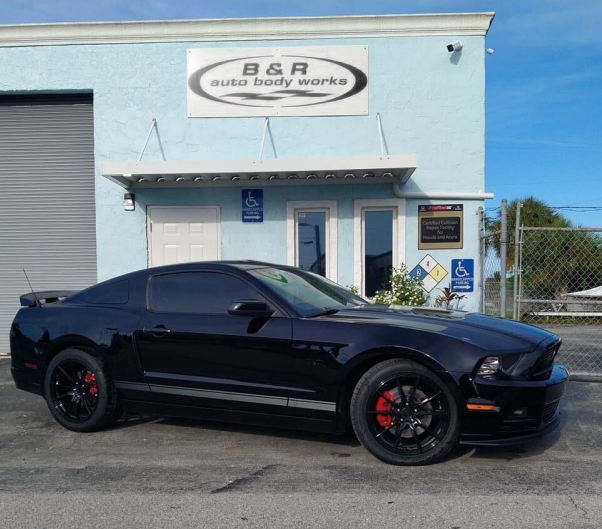 A black car is parked in front of a building that says b & r auto body works | B & R Auto Body Works