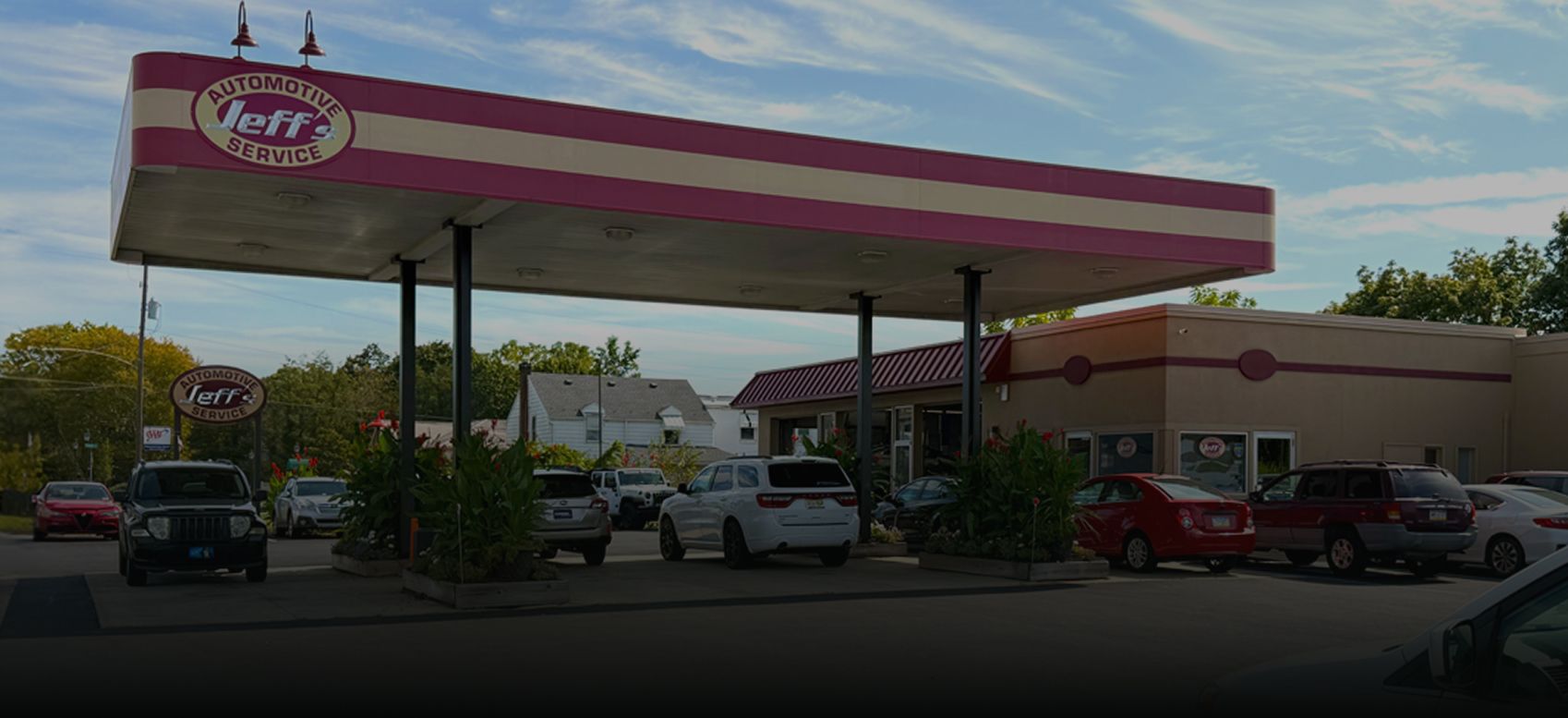 Convenience store gas station with red-and-white canopy and parked cars under a partly cloudy sky