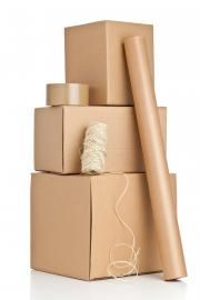 Stacked cardboard boxes with a roll of packing paper, a roll of tape, and a spool of twine on a white background.