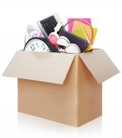 A cardboard box filled with miscellaneous items including a clock, headphones, notebooks, and a calculator.