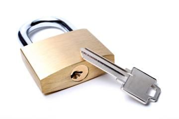 A brass padlock with a silver shackle lying next to a metal key on a white background.