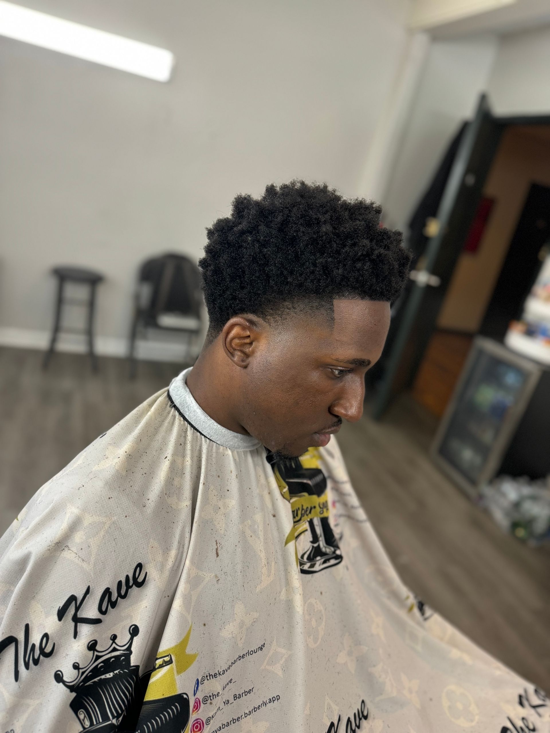 Man with short, textured hair and a fade haircut, wearing a barber cape in a shop setting.