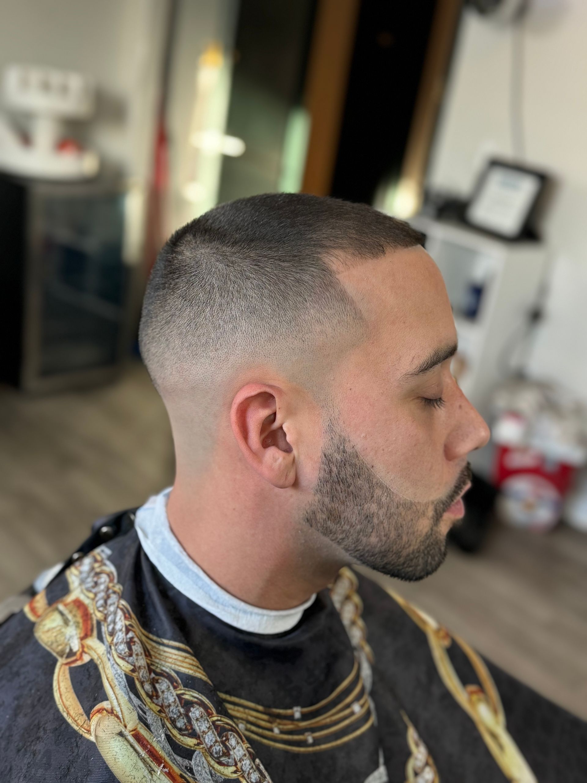 Man with a faded haircut and beard. He is wearing a barber cape.