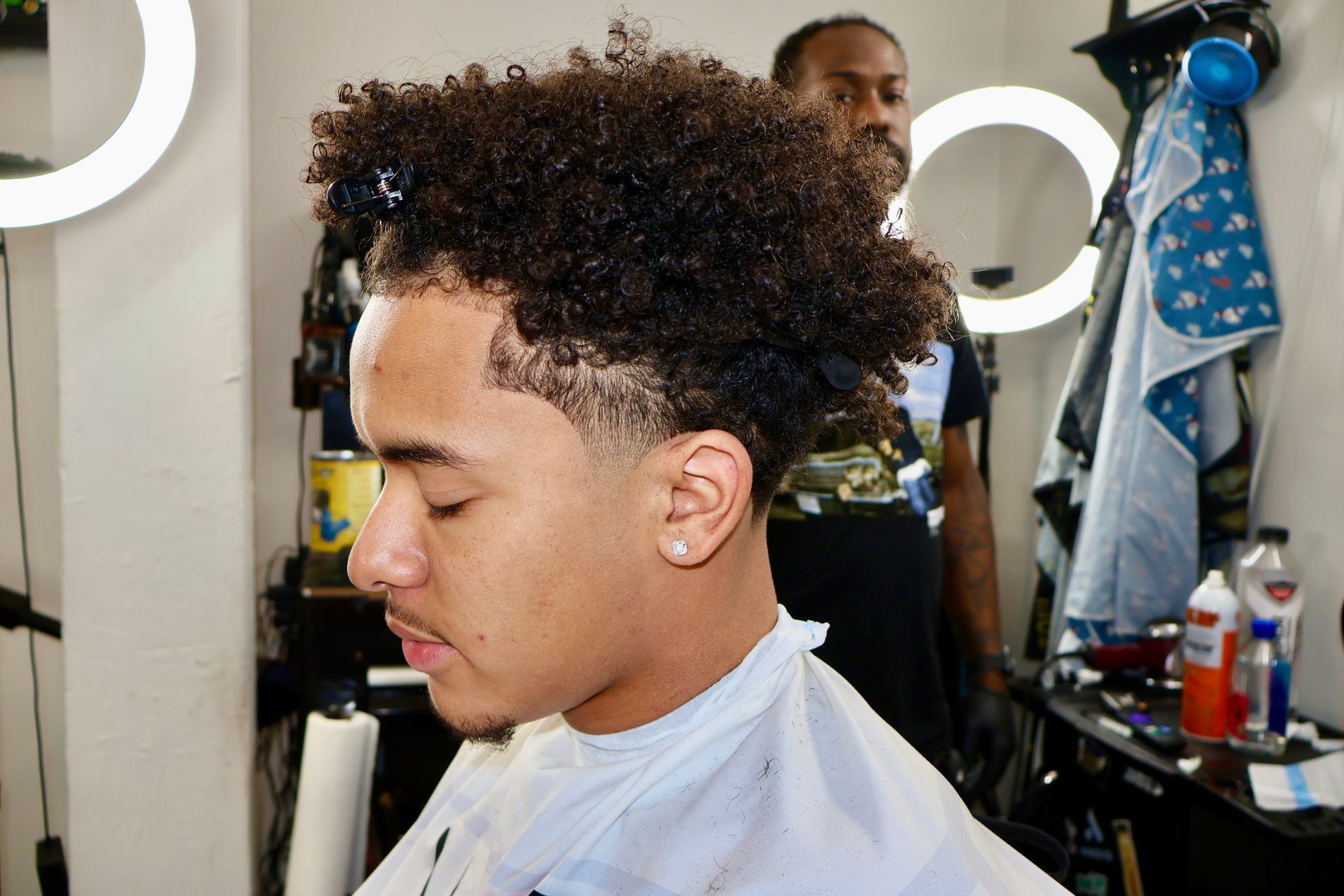 A person getting a haircut in a barber shop, side view. The barber is behind the subject.