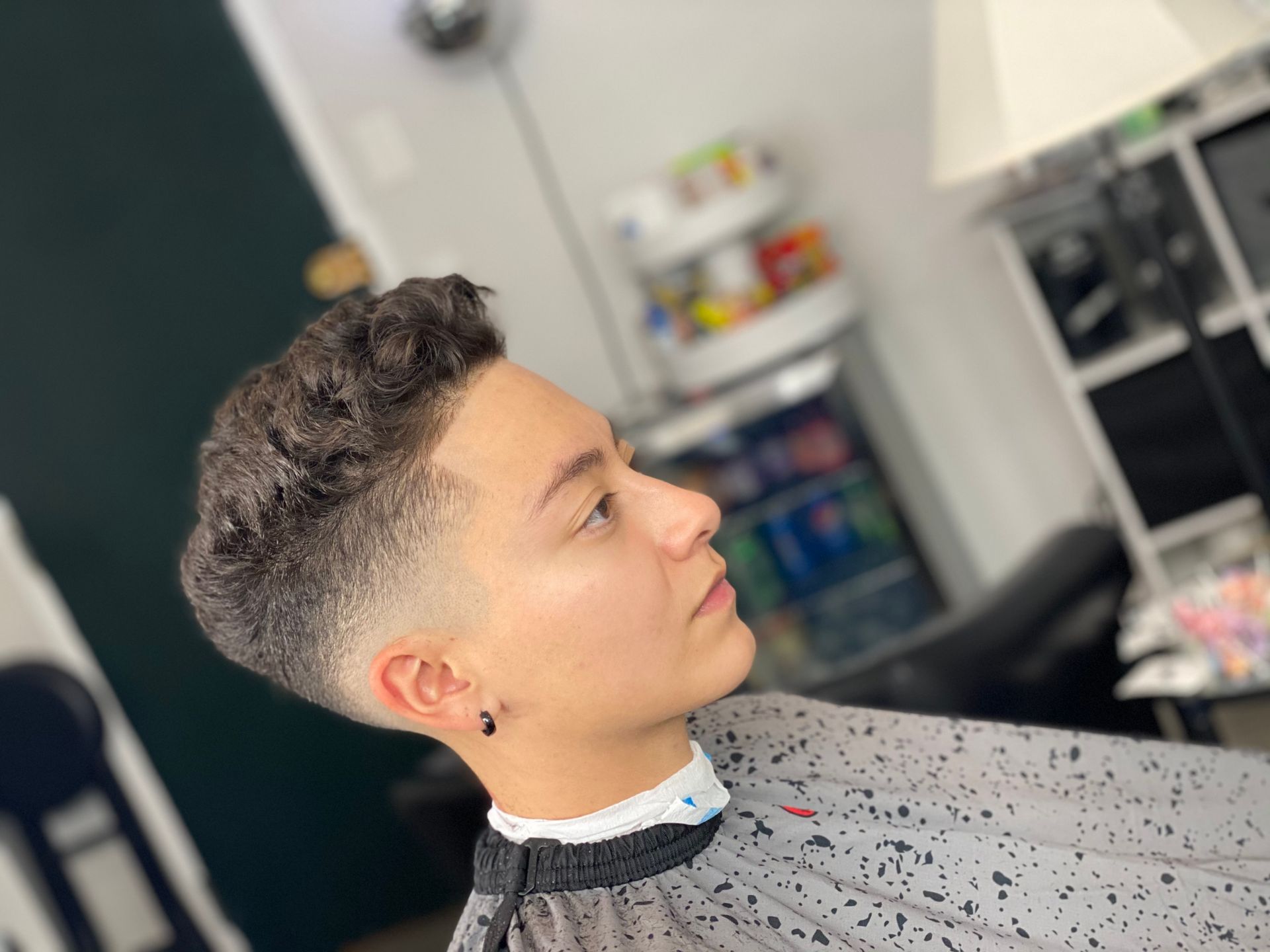 Person with a faded haircut at a salon. The hair is dark and curly on top, fading to the skin on the sides.