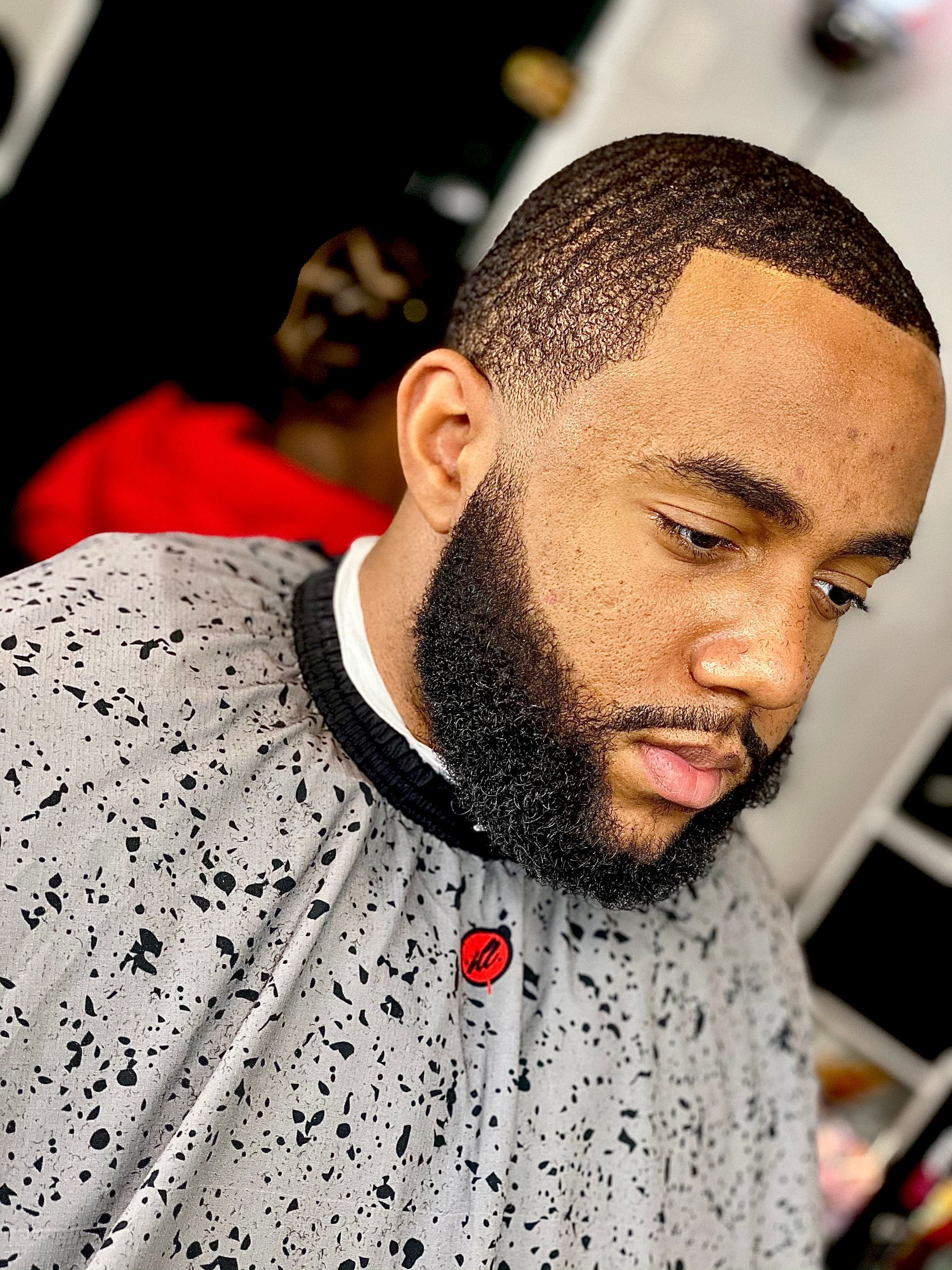 Man with short dark hair and beard, wearing a gray speckled barber cape.