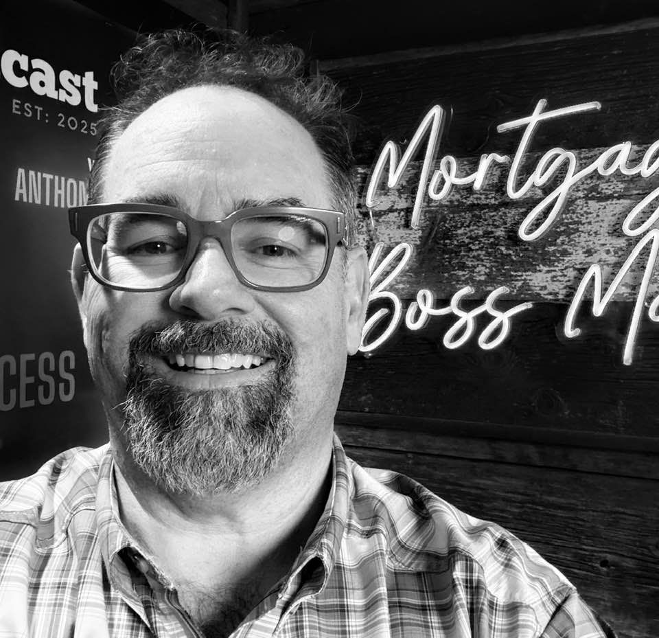 A man with glasses and a beard is smiling in a black and white photo.