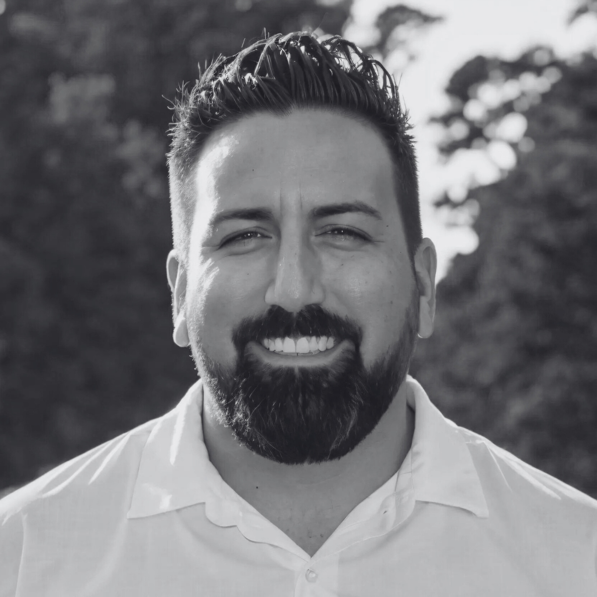 A man with a beard is smiling in a black and white photo.