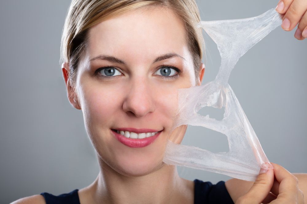 Close Up Of A Smiling Woman Peeling Off A Facial Mask — Jina Robinson Skin-Cos-Medix In Albion Park NSW
