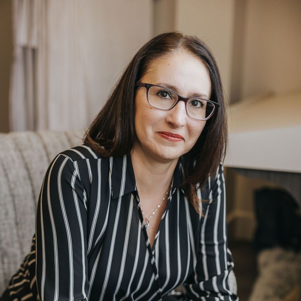 A woman wearing glasses and a striped shirt is sitting on a couch.