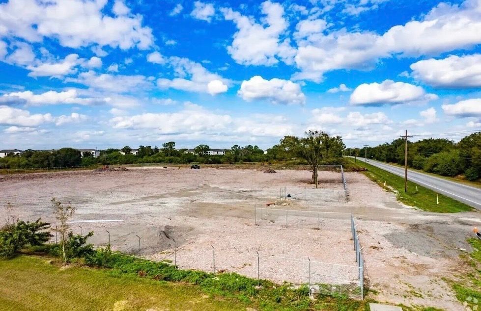 Open field of gravel under a blue sky, with a road and few trees in the distance.