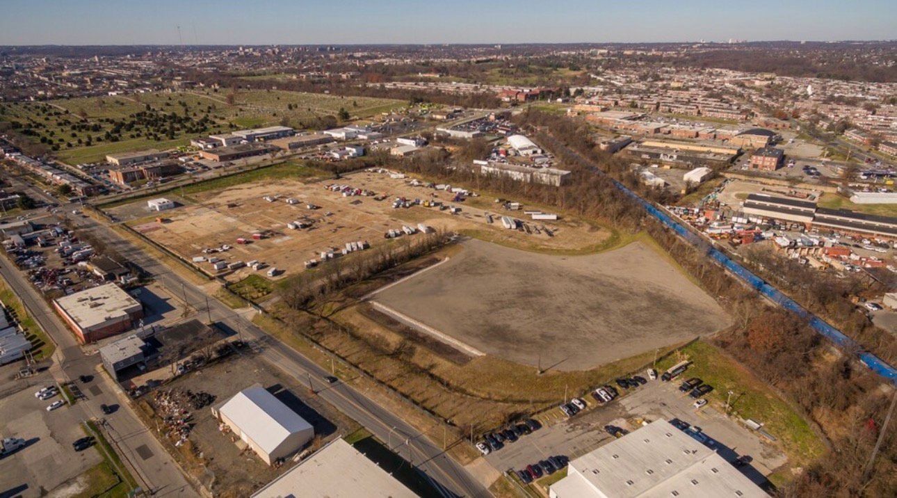 Aerial view of a large, mostly empty lot surrounded by buildings and a road, under a clear sky.