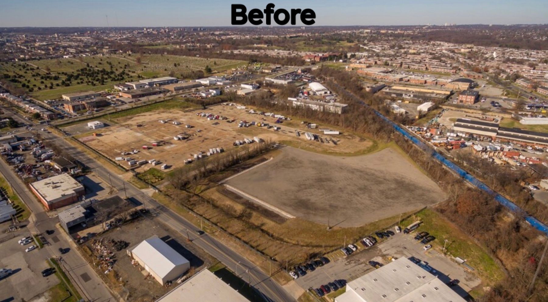 Aerial view of a vacant lot next to a railway and urban area; mostly brown and gray tones, trees present.