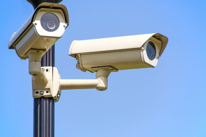 Two white outdoor security cameras mounted on a pole against a blue sky.