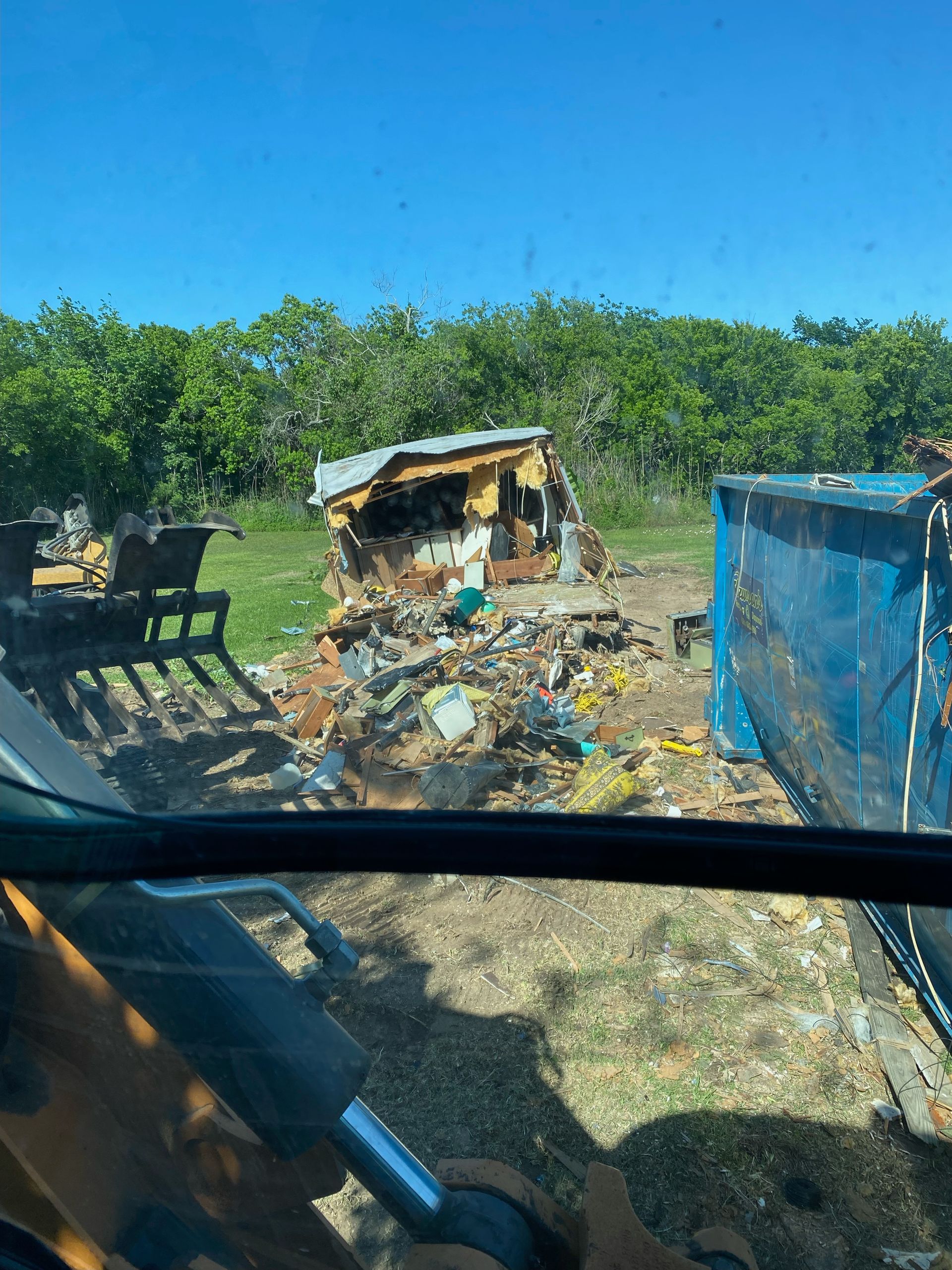 A person is driving a bulldozer in a field with a house in the background.