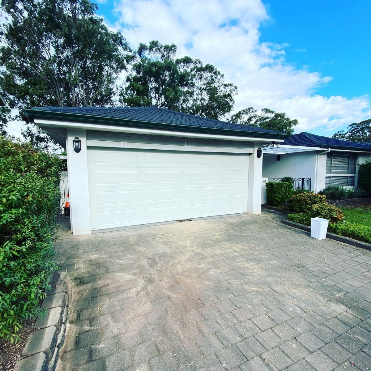 White garage with a dark roof and a brick driveway.