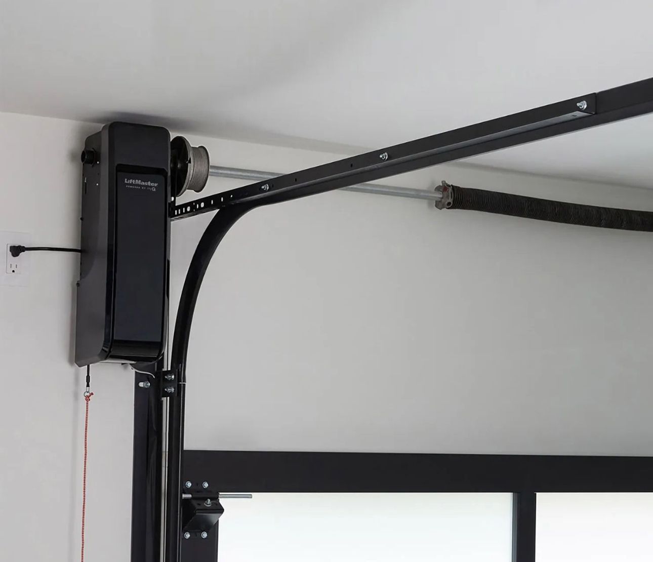 Garage door opener mounted on white ceiling. Metal arm connects to door.