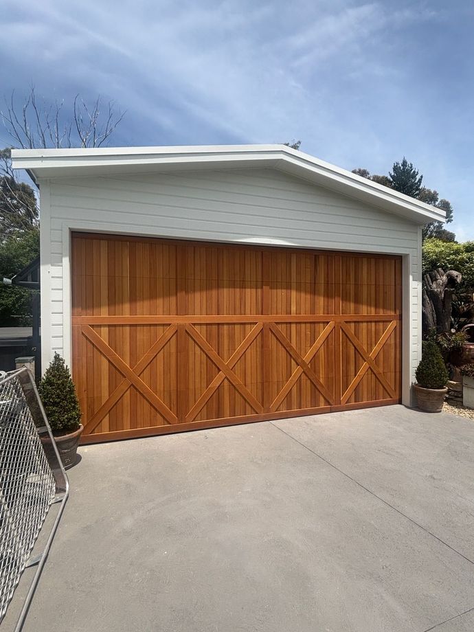 Two beige garage doors on a light gray house with dark driveway. A van is parked on the left.