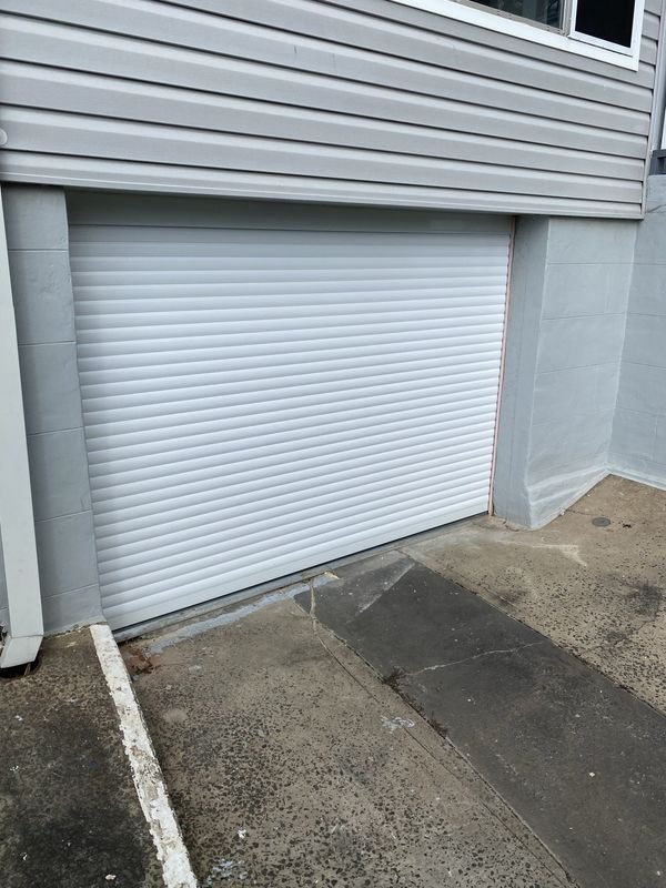 White roll-up garage door in a gray concrete alcove, below gray siding.