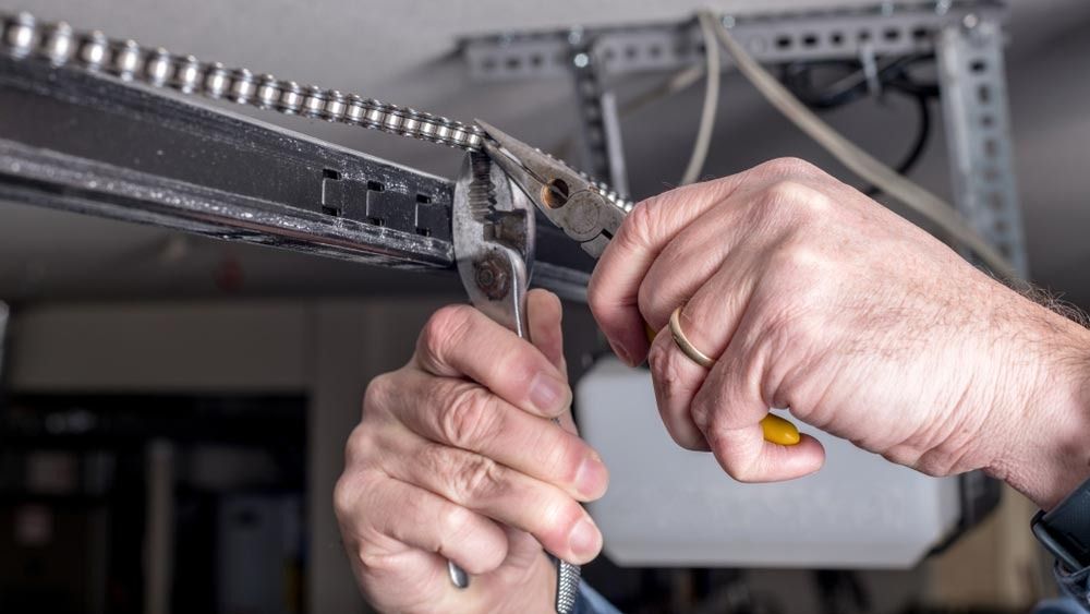 Person's hands using pliers and wrench to repair a garage door opener chain.