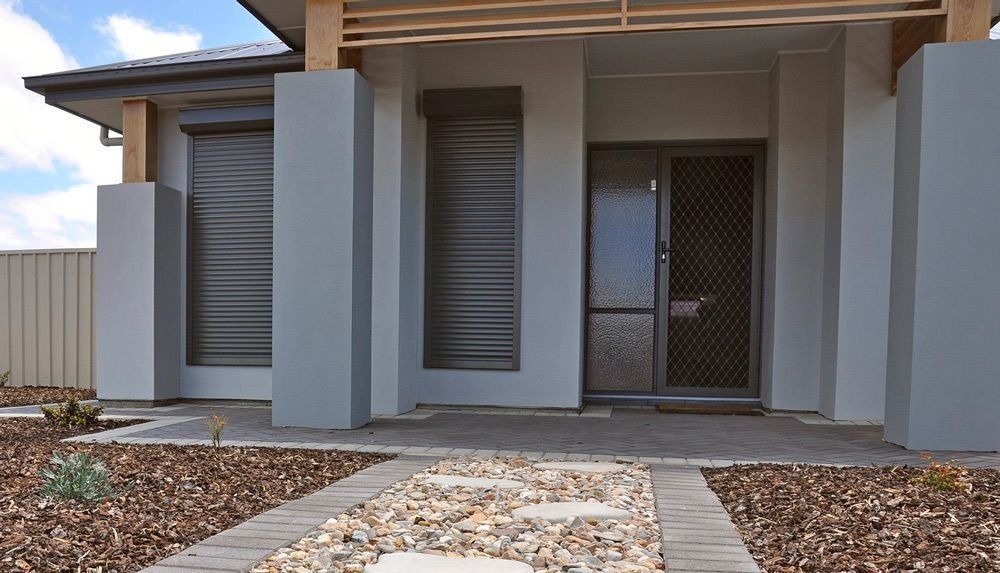 Gray house exterior with stone pathway, front door, and shuttered windows.