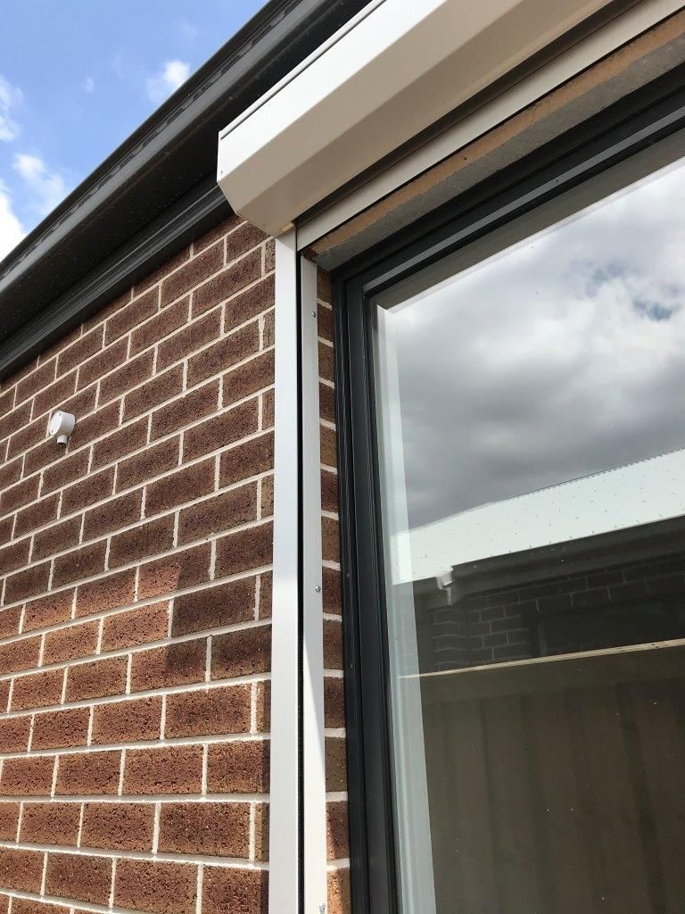 Exterior view of a window with a beige roller shutter. Red brick wall and dark window frame. Blue sky.
