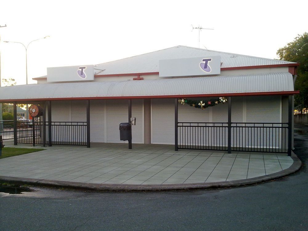 Building with Telstra logos; white exterior, red trim, black railings, and a paved area.