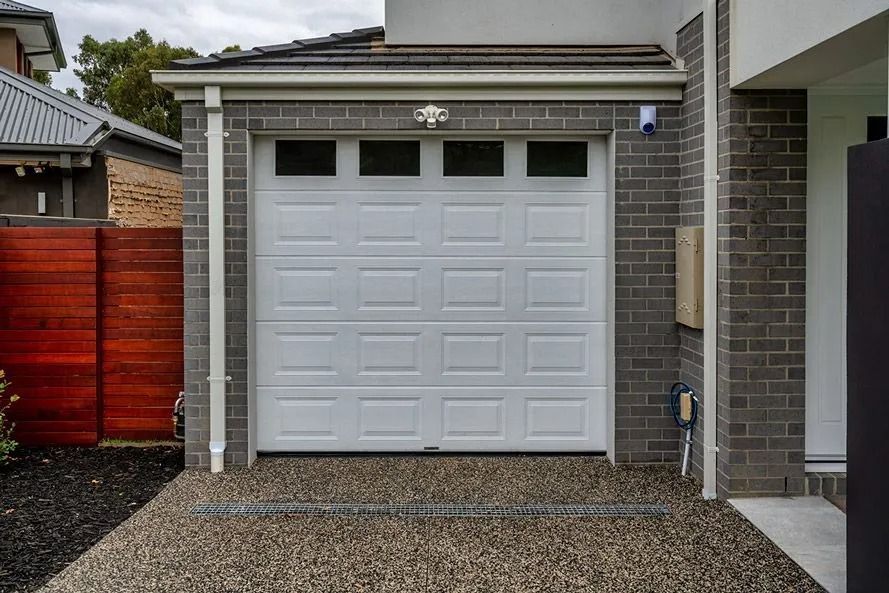 White garage door with four small windows, set in a brick facade, driveway with gravel.