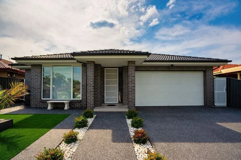 Modern brick house with garage, large window, and stone walkway under a blue sky.