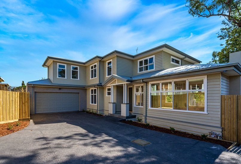 Two-story brick house with garage. A worker on a ladder paints the column under the porch, blue sky.
