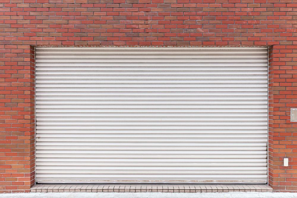 Tan garage door with windows above, on a yellow house. Concrete driveway.